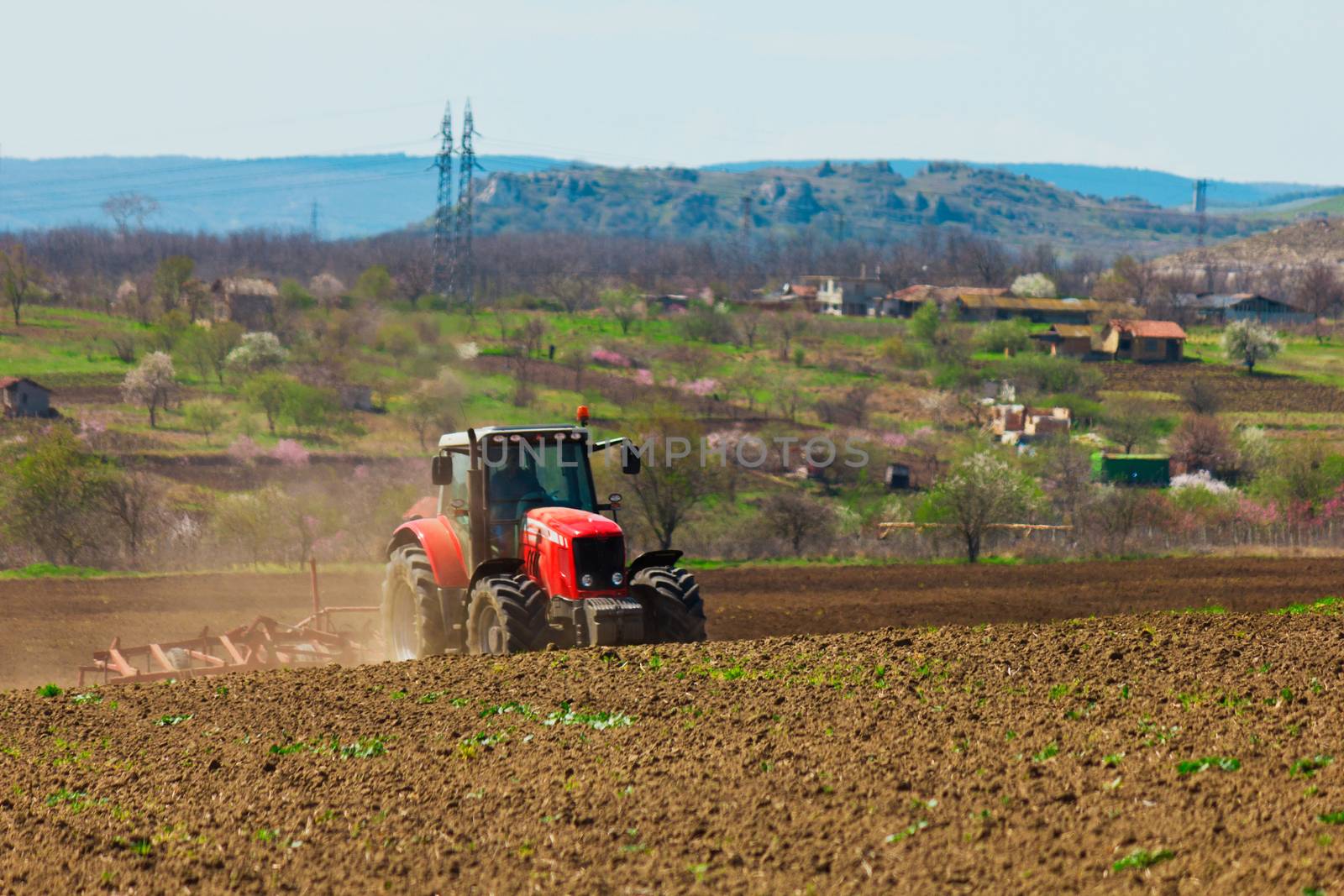 Farmer plowing the field. Cultivating tractor in the field. Red farm tractor with a plow in a farm field. Tractor and Plow