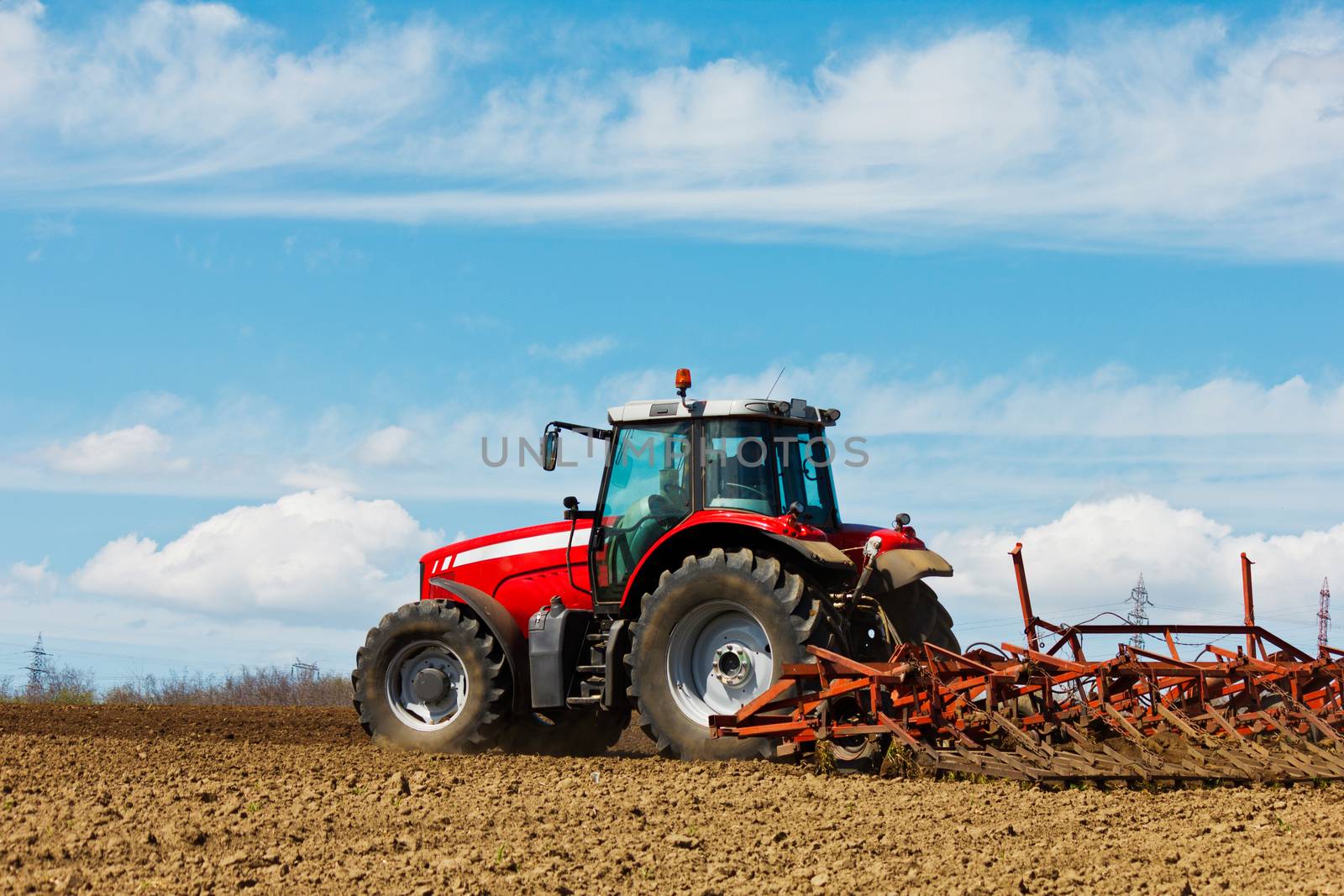 Farmer plowing the field. Cultivating tractor in the field. Red farm tractor with a plow in a farm field. Tractor and Plow