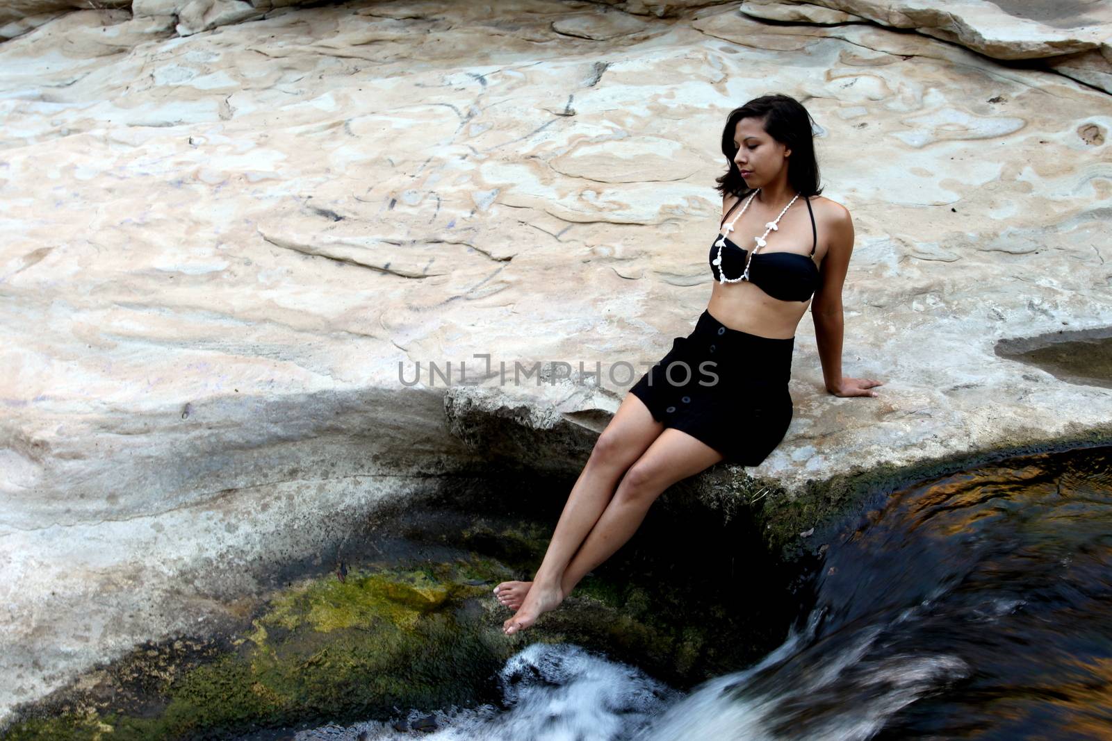 Hispanic woman with bikini lying next to a waterfall.