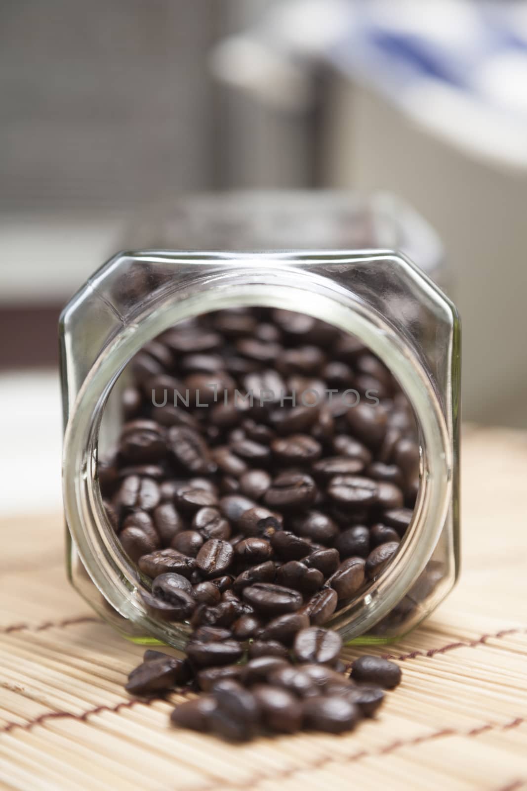 Coffee beans spilled from glass bottle on a wooden table top.