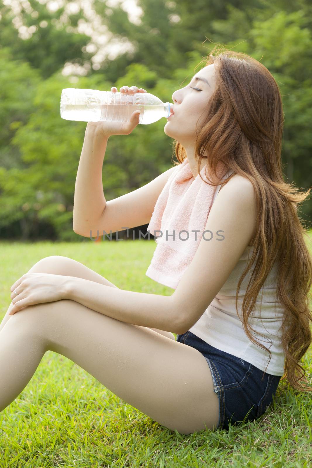 Woman sit and drink after exercise. On the lawn after a workout in the park.