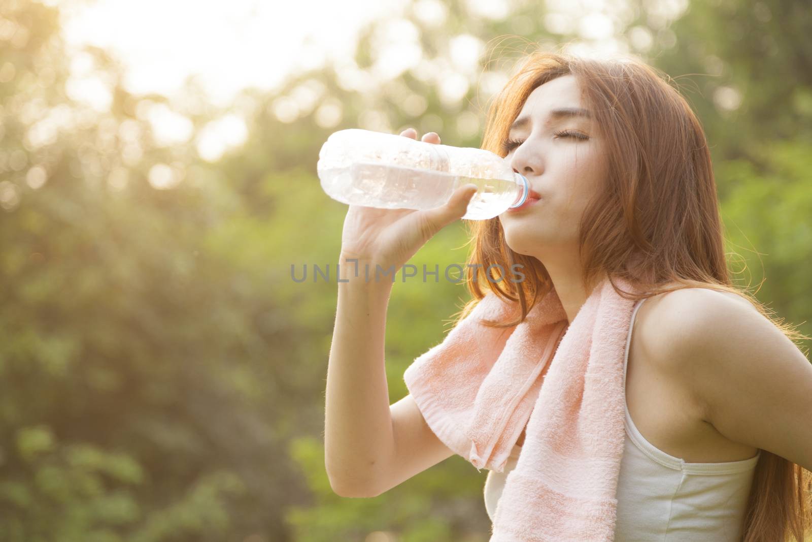 Woman sit and drink after exercise. On the lawn after a workout in the park.