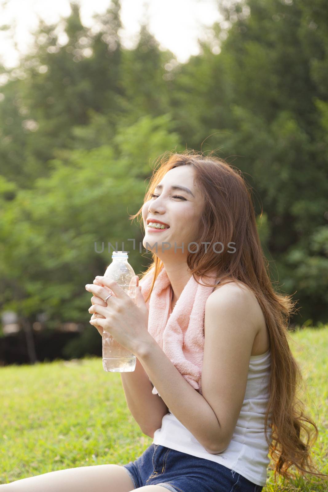 Woman sitting rest after exercise. Hand holding a bottle of water and sit On the lawn.