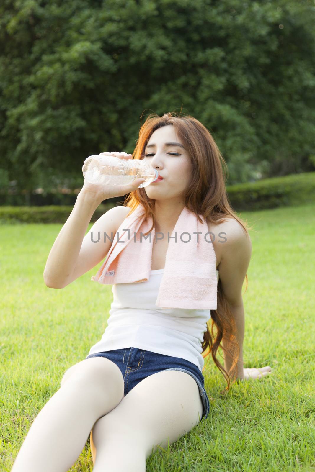 Woman drinking water and sit on grass. After jogging in the evening.