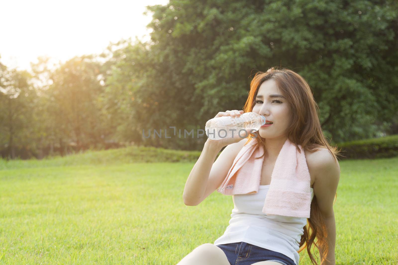 Woman drinking water and sit on grass. After jogging in the evening.