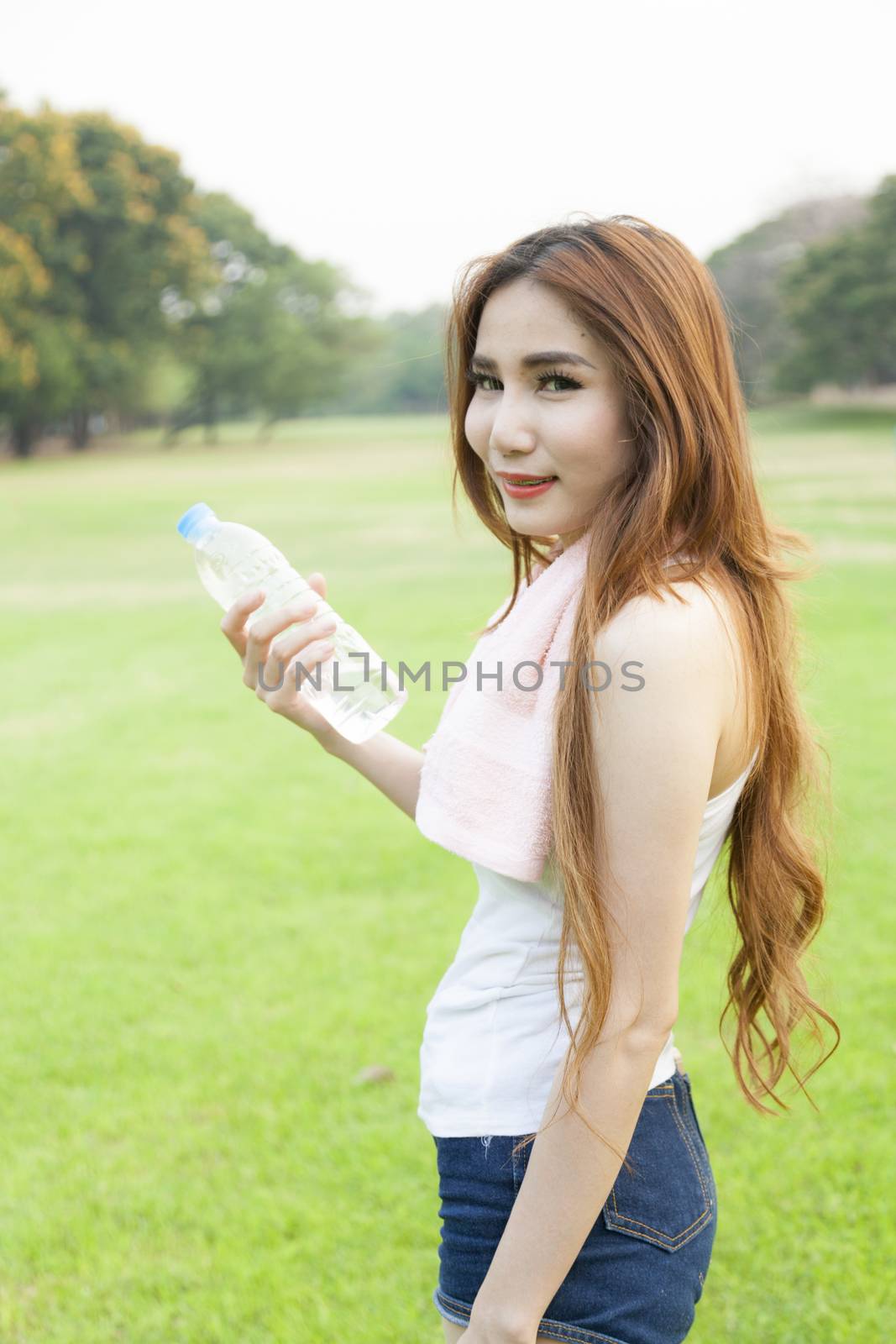 Woman holding a bottle of water. Jogging on grass in the park.