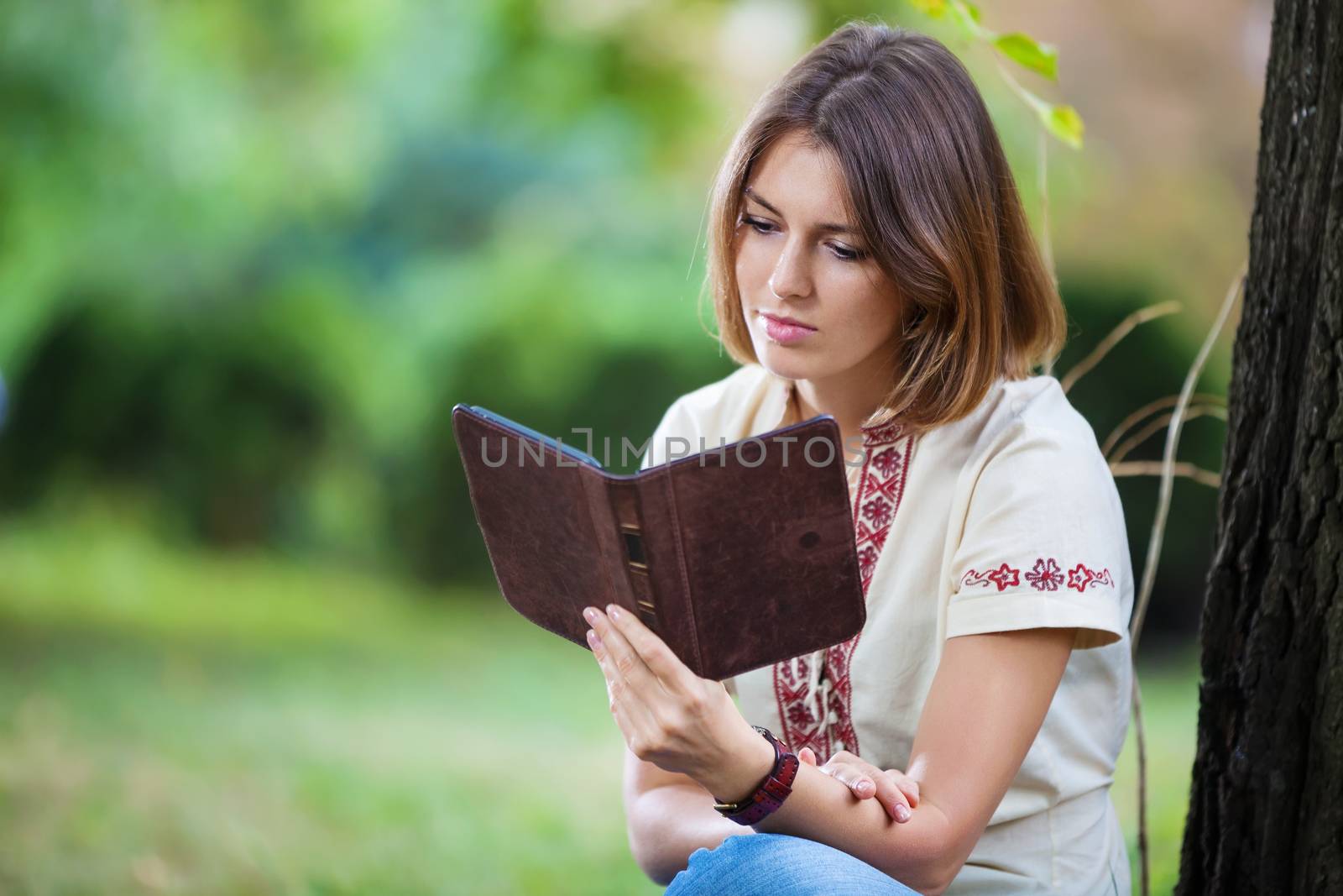Young attractive woman reading e-book in park by photobac