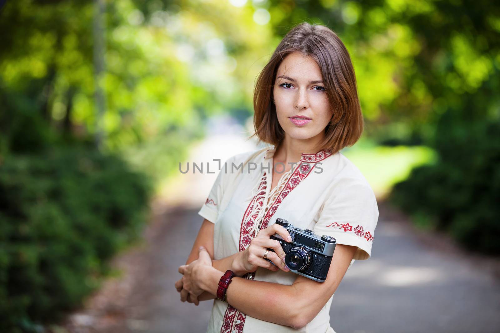Young woman holding retro style camera in park by photobac
