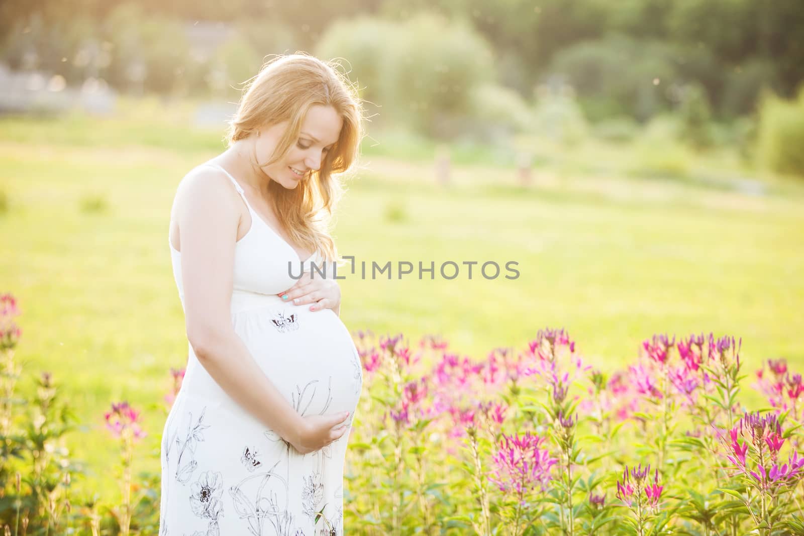 Young pregnant woman looking at her belly and smiling in a park