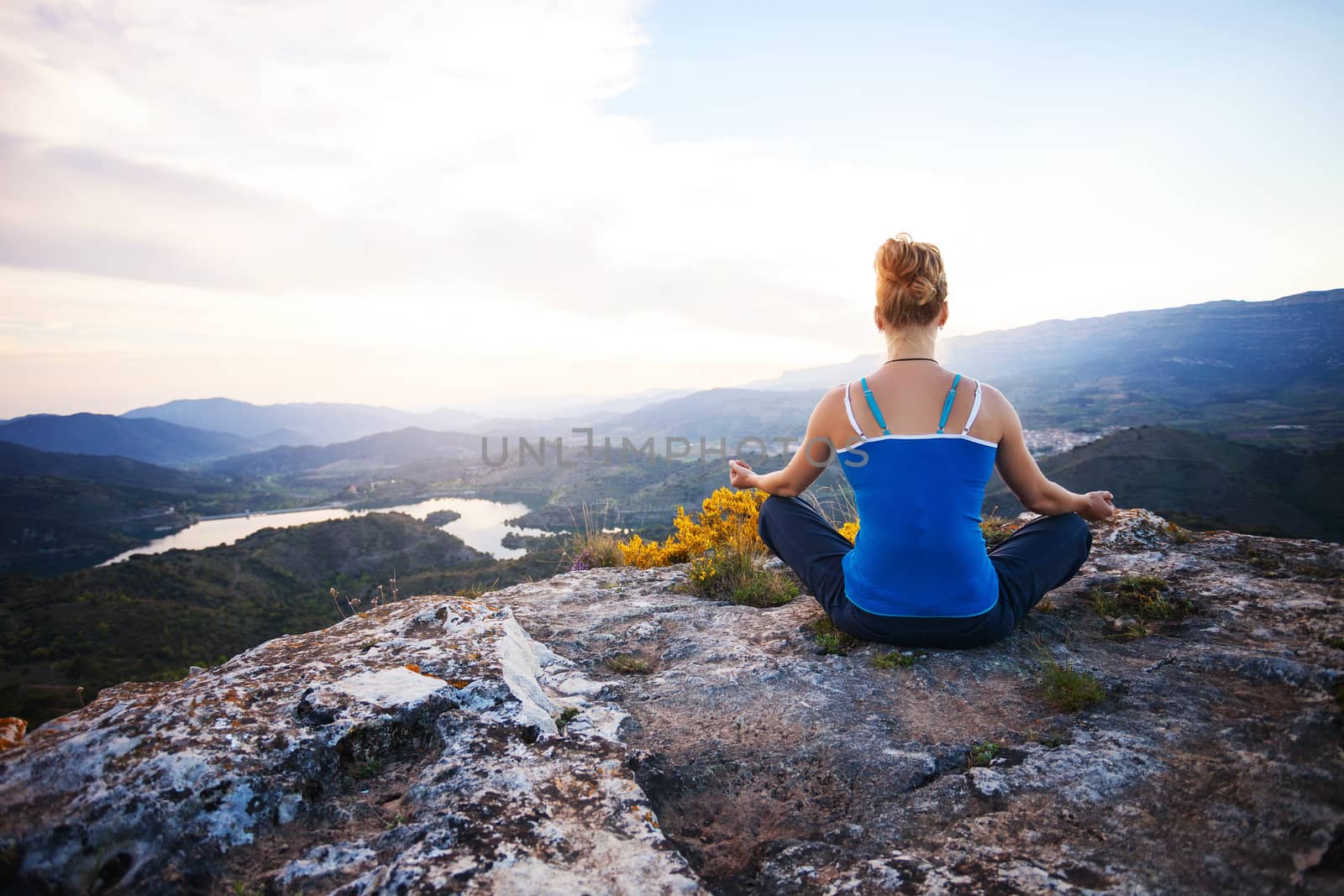 Young woman sitting on a rock and enjoying valley view. Girl sits in asana position.