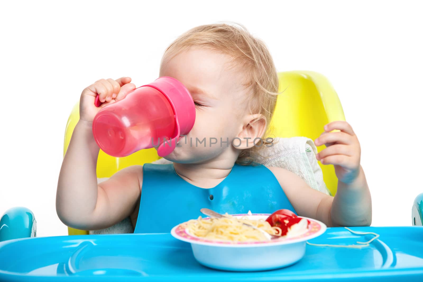 Little boy drinking water while sitting at table with plate of spaghetti