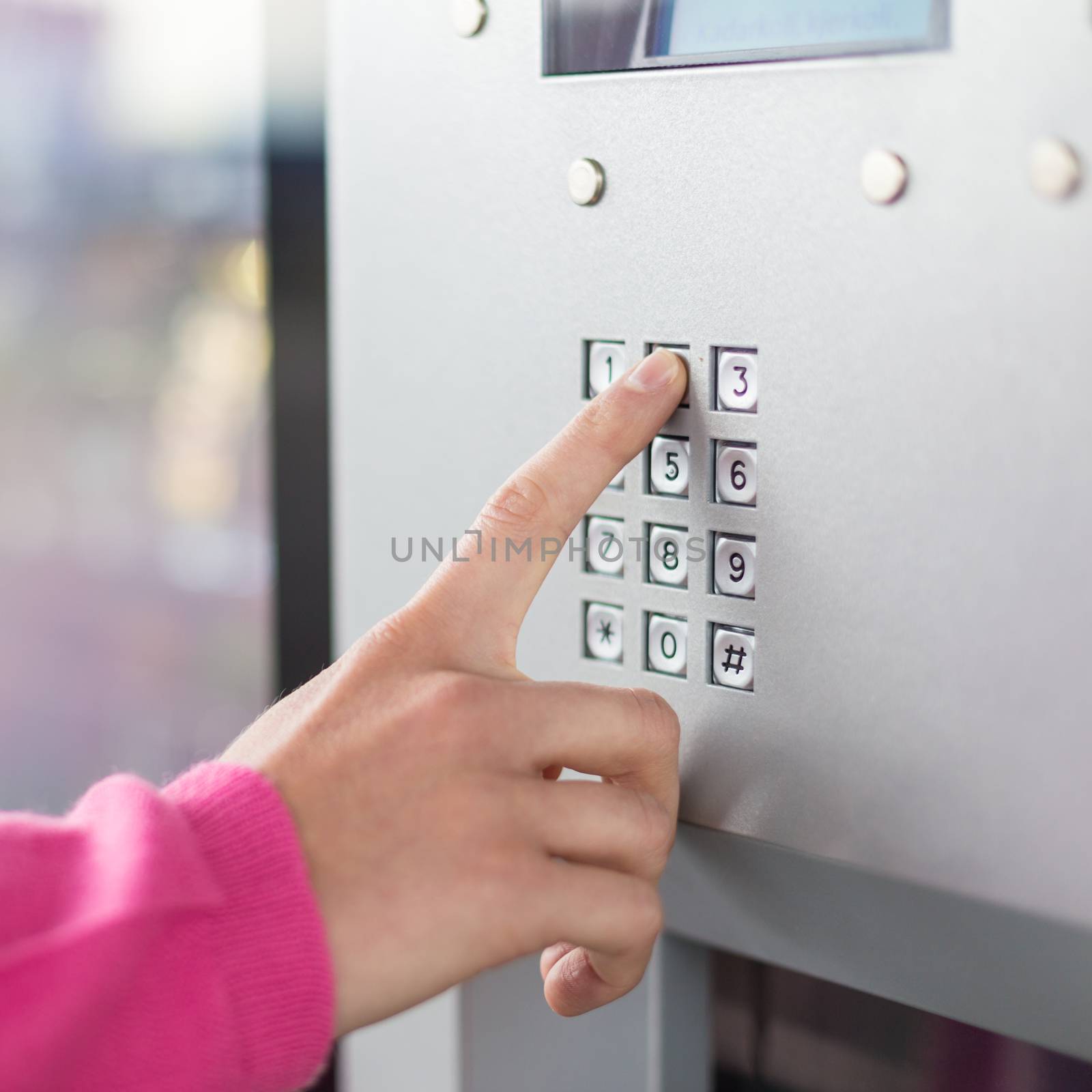 Women's hand using a dial pad on a machine. The fore finger is placed on the dial pad key and is about to press on that. Small sized display with blue background light is also visible.