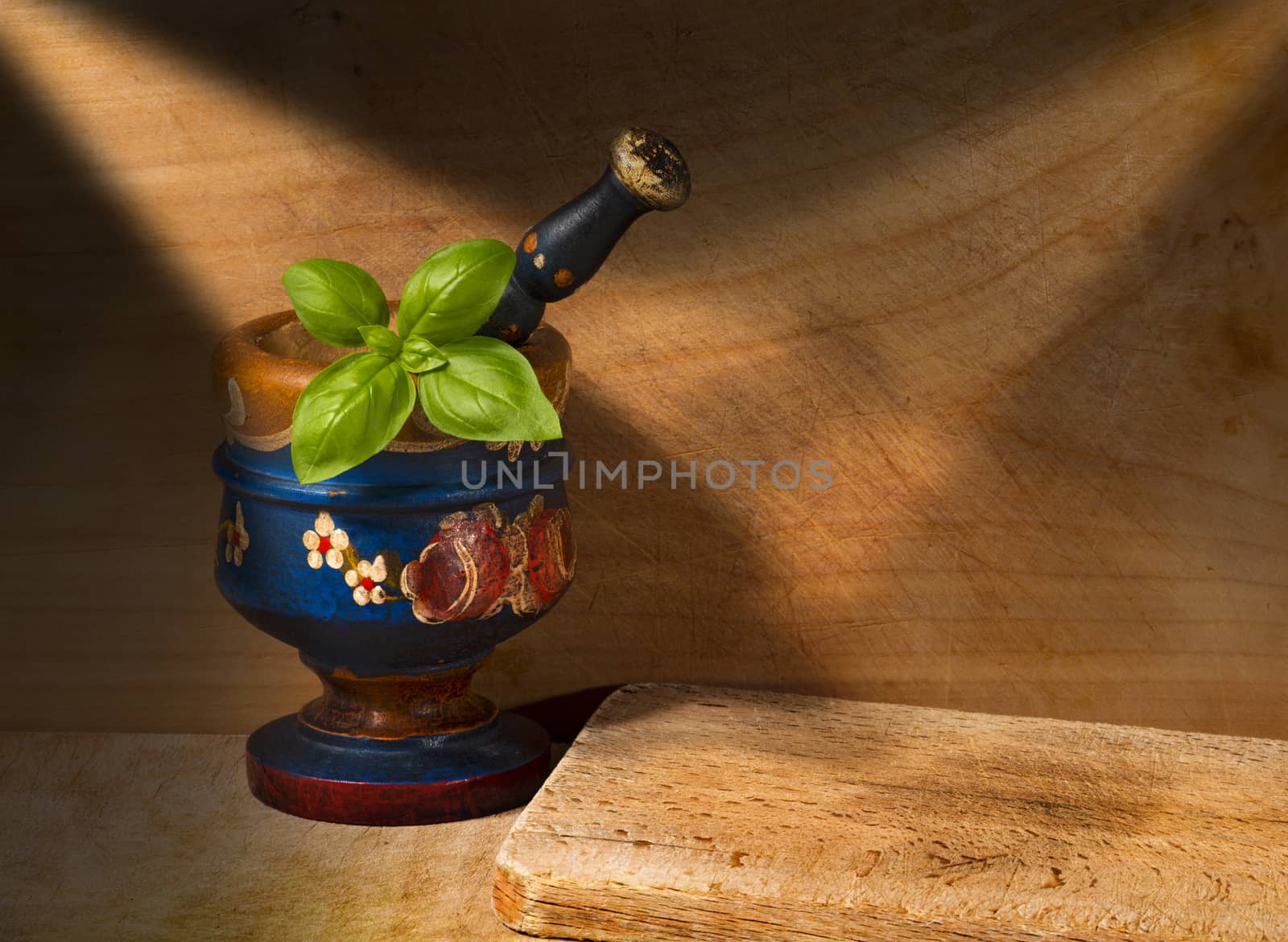 Old wooden mortar and pestle with basil leaves on wooden wall with chopping board
