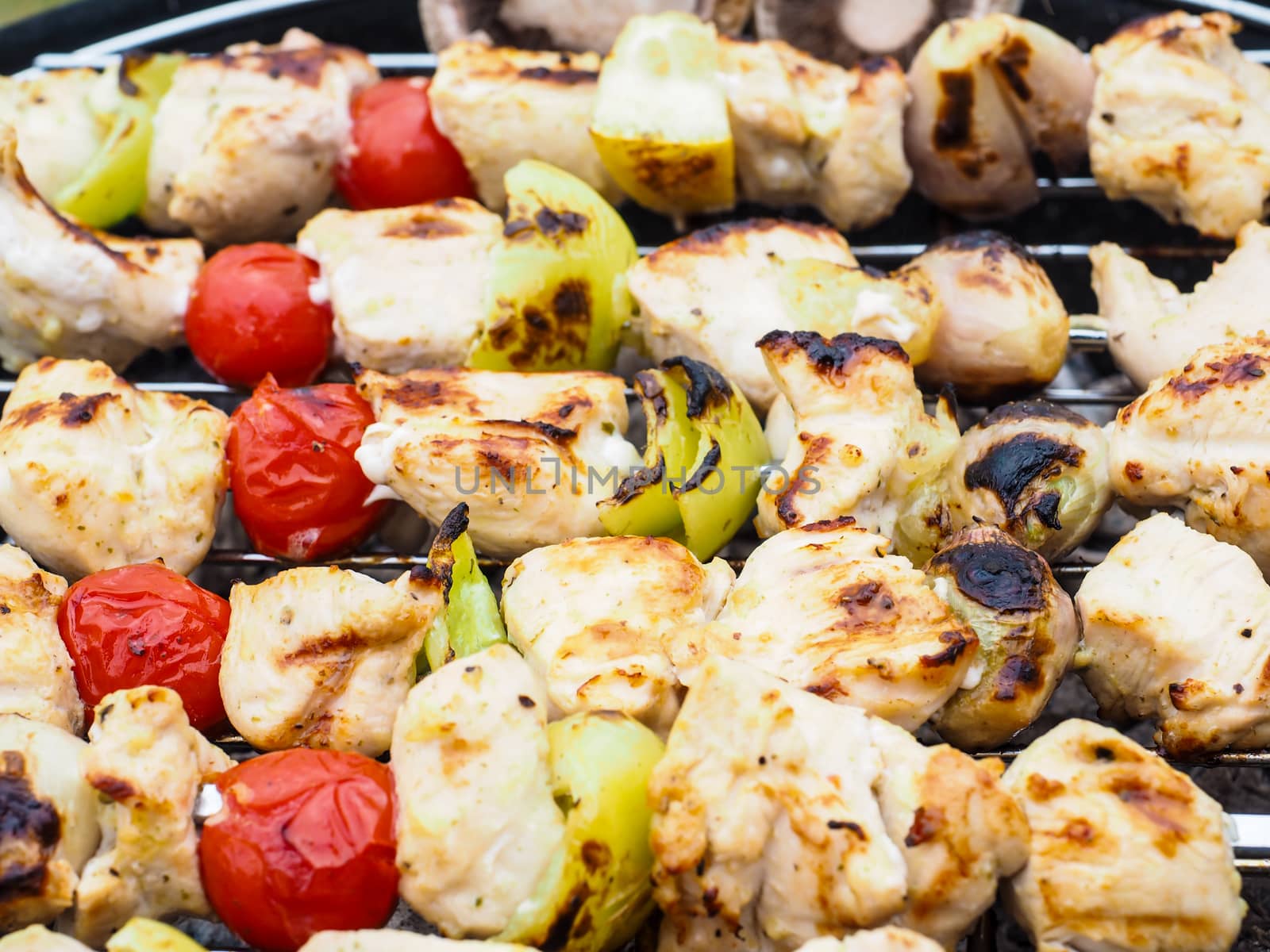 Barbecuing chicken, vegetables on spear over charcoal grill by Arvebettum