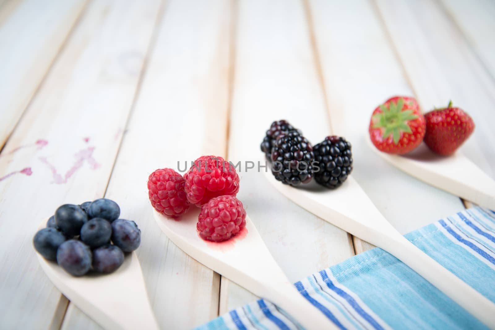 fresh organic berrys fruits on wooden spoon over blue kitchen cloth on white background retro style wooden table