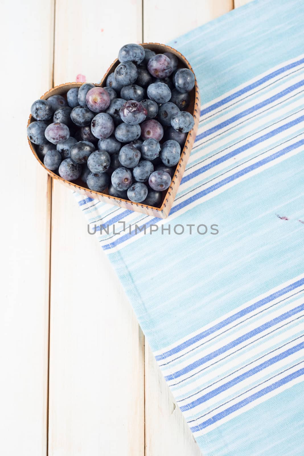 fresh organic blueberries in heart style shape basket and blue kitchen cloth on white background retro kitchen table