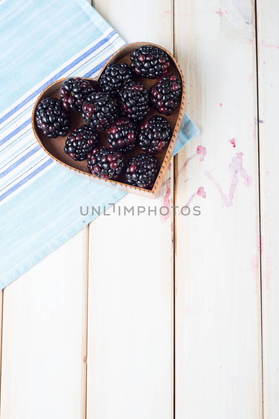 fresh organic blackberries in heart style shape basket  on white background retro kitchen table and blue kitchen cloth