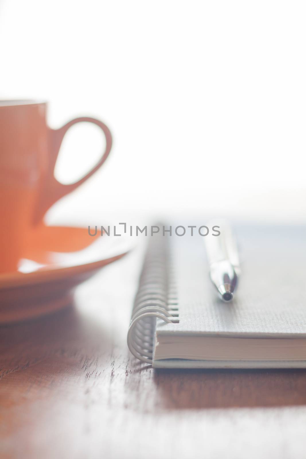 Orange coffee cup, pen and notebook on wooden table by punsayaporn