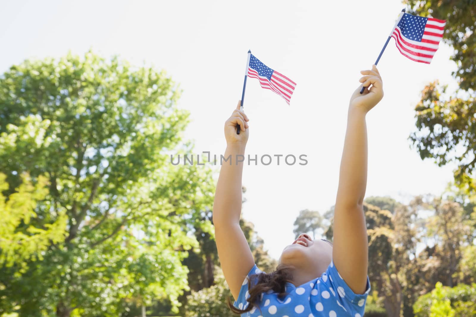 Girl holding up two American flags at park by Wavebreakmedia