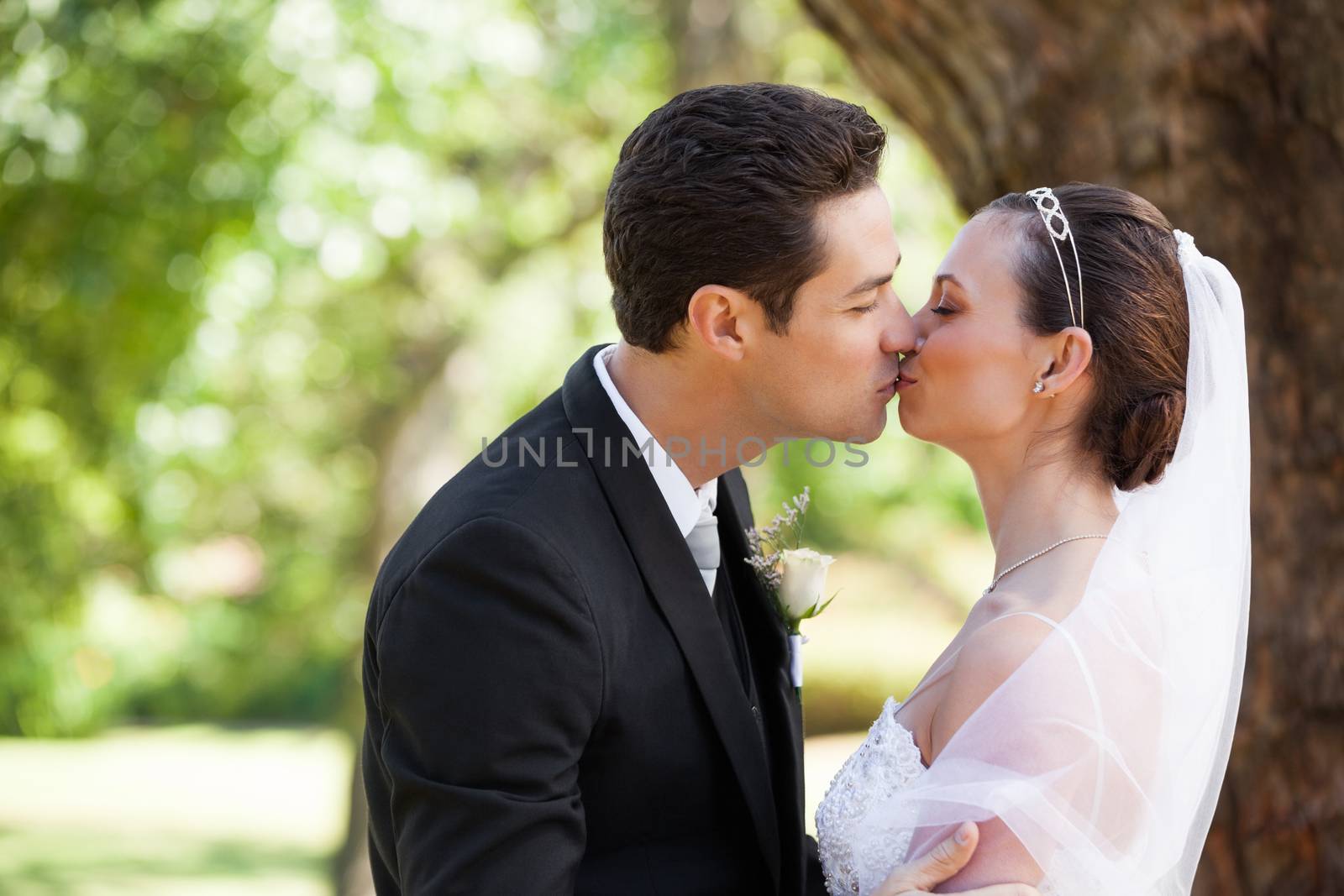 Side view of a romantic newlywed couple kissing in the park