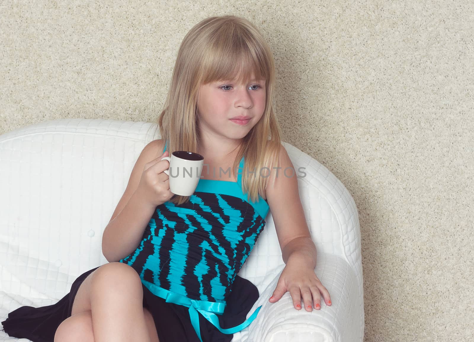 Girl 5 years old sitting on a sofa in a dress with a cup in hands