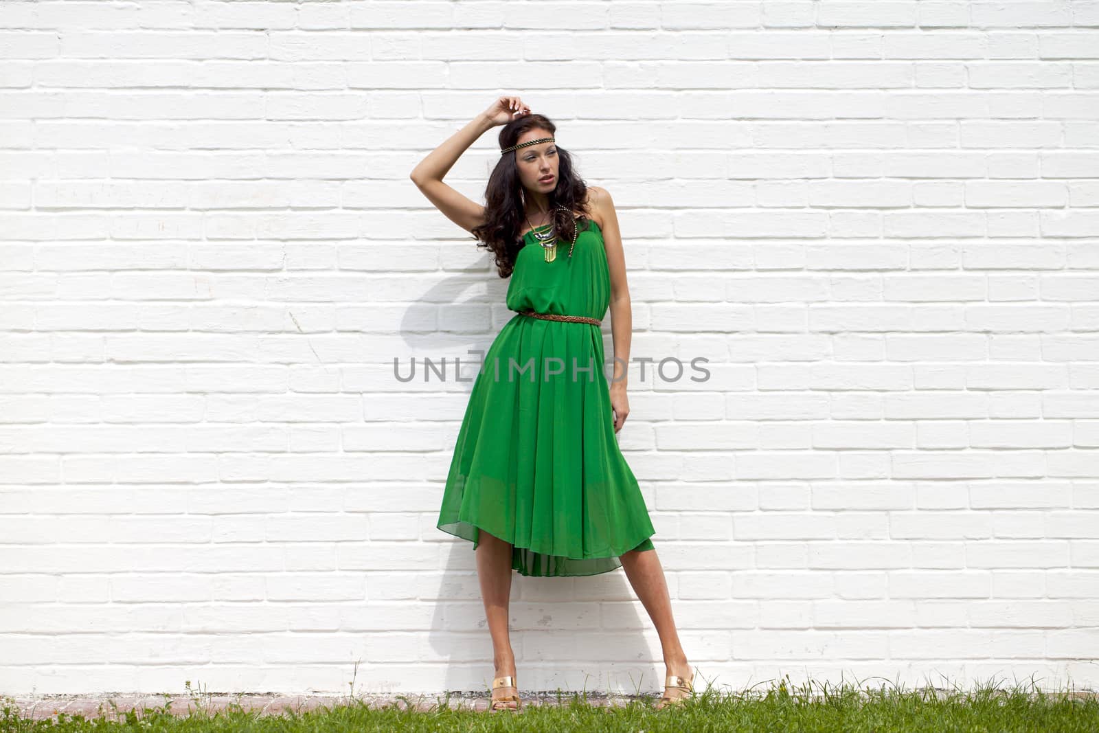 Beautiful young woman in green dress, against white wall