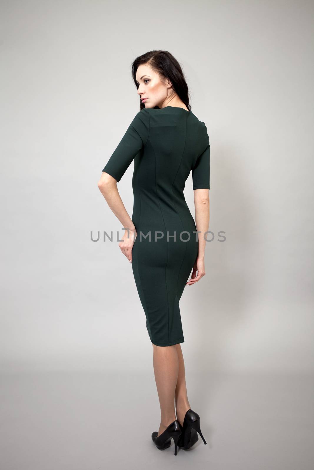 Young beautiful caucasian brunette in green dress posing on grey background