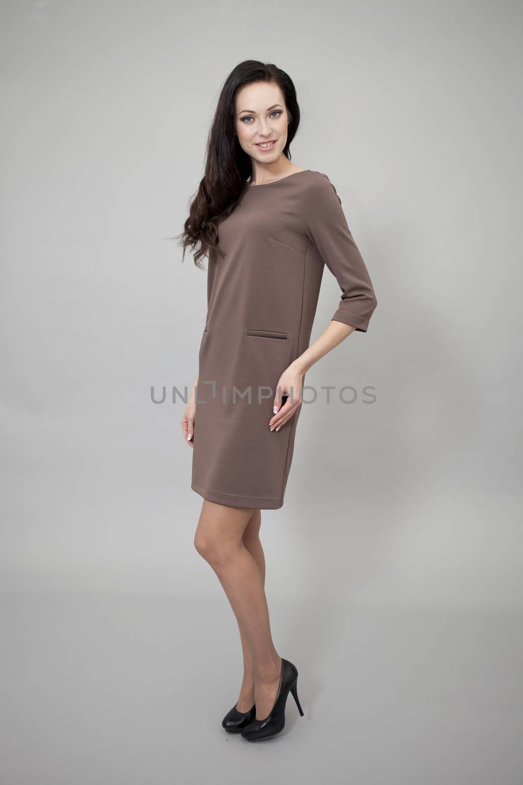 Young beautiful caucasian brunette in fashion dress posing on grey background