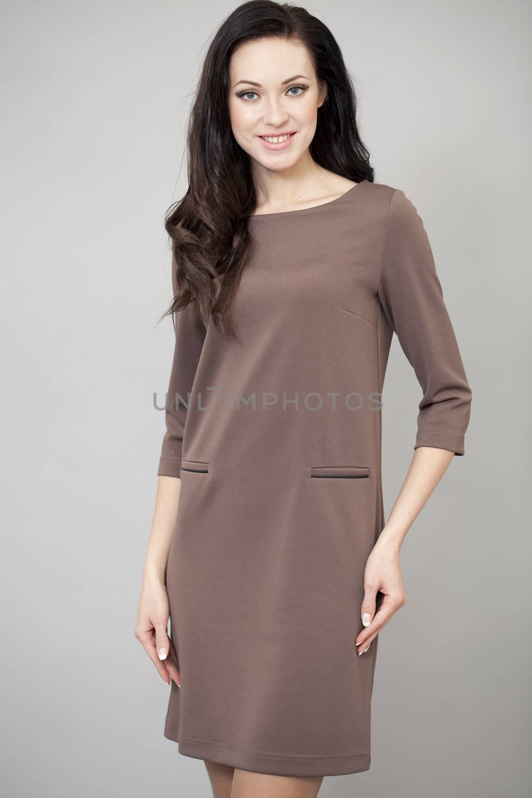 Young beautiful caucasian brunette in fashion dress posing on grey background