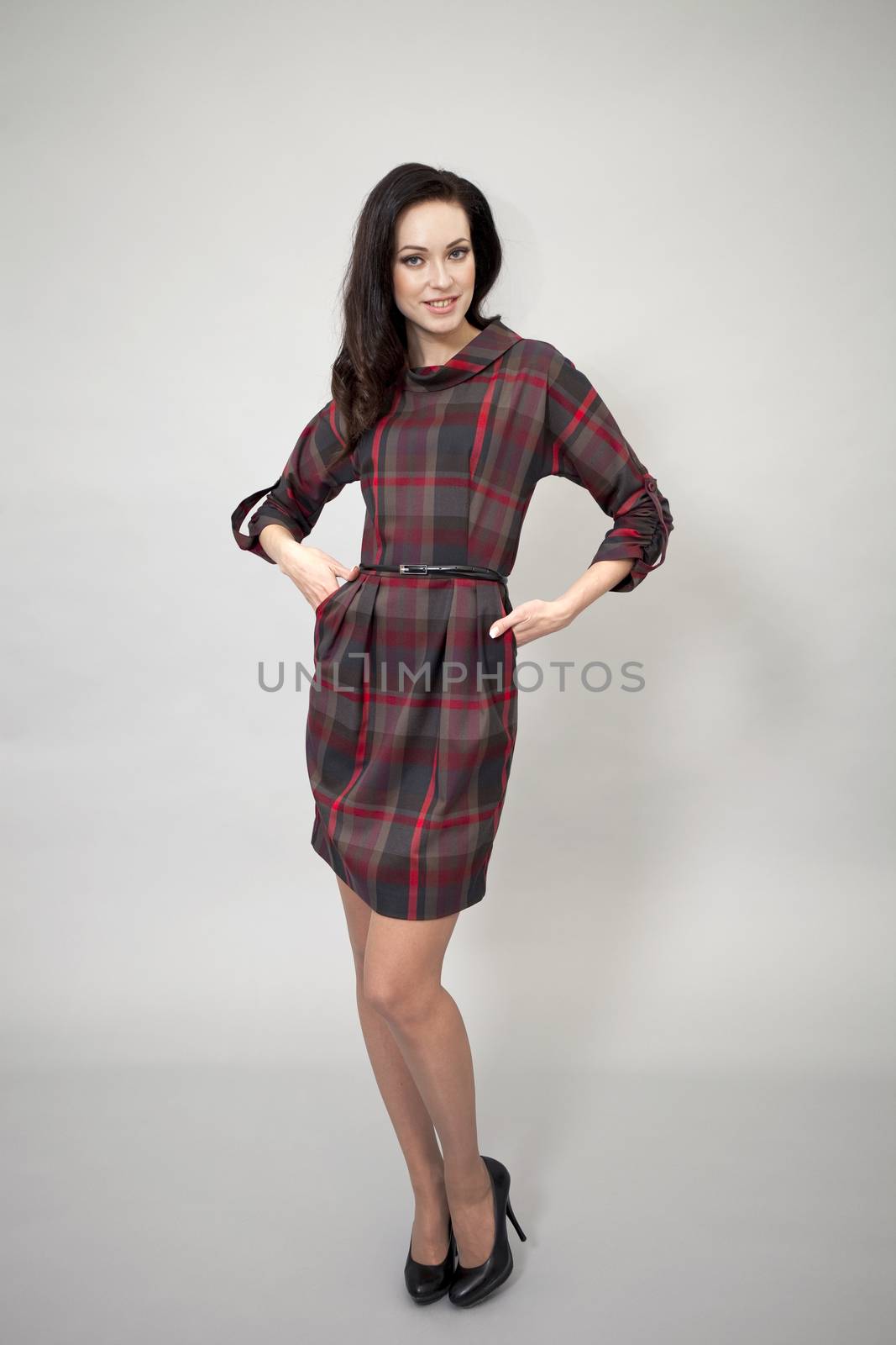 Young beautiful caucasian brunette in fashion dress posing on grey background