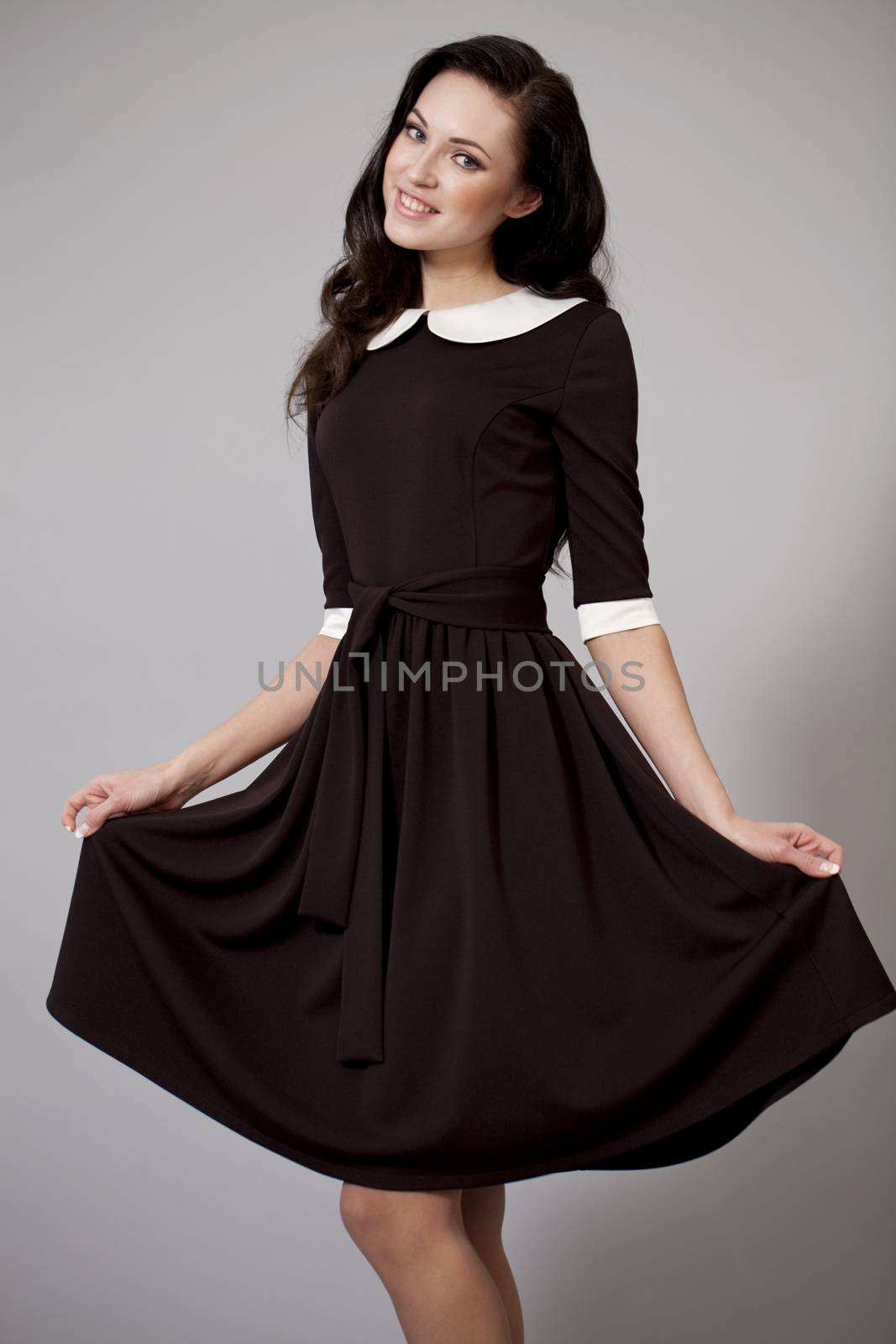 Young beautiful caucasian brunette in fashion dress posing on grey background