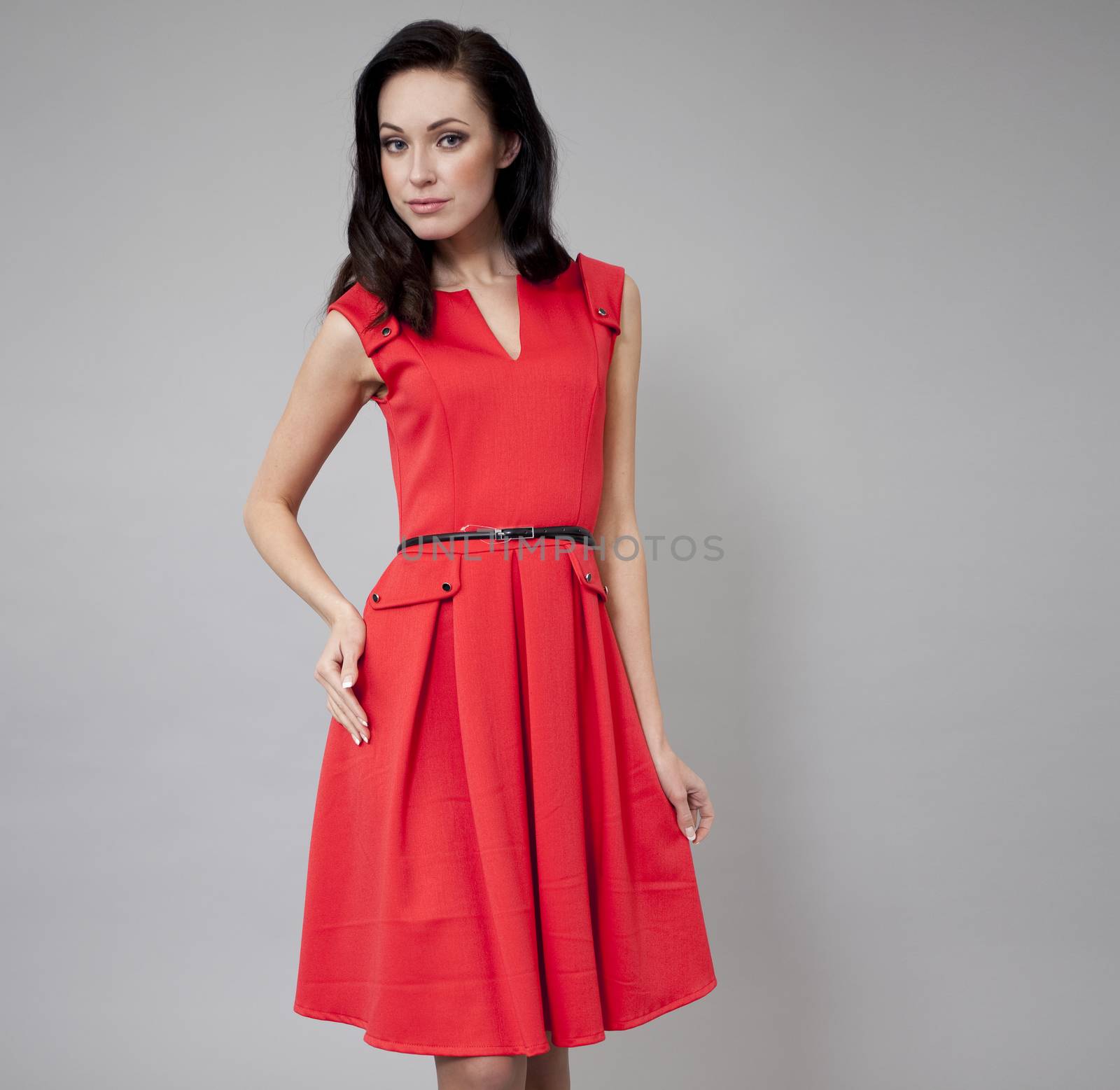 Young beautiful caucasian brunette in red dress posing on grey background