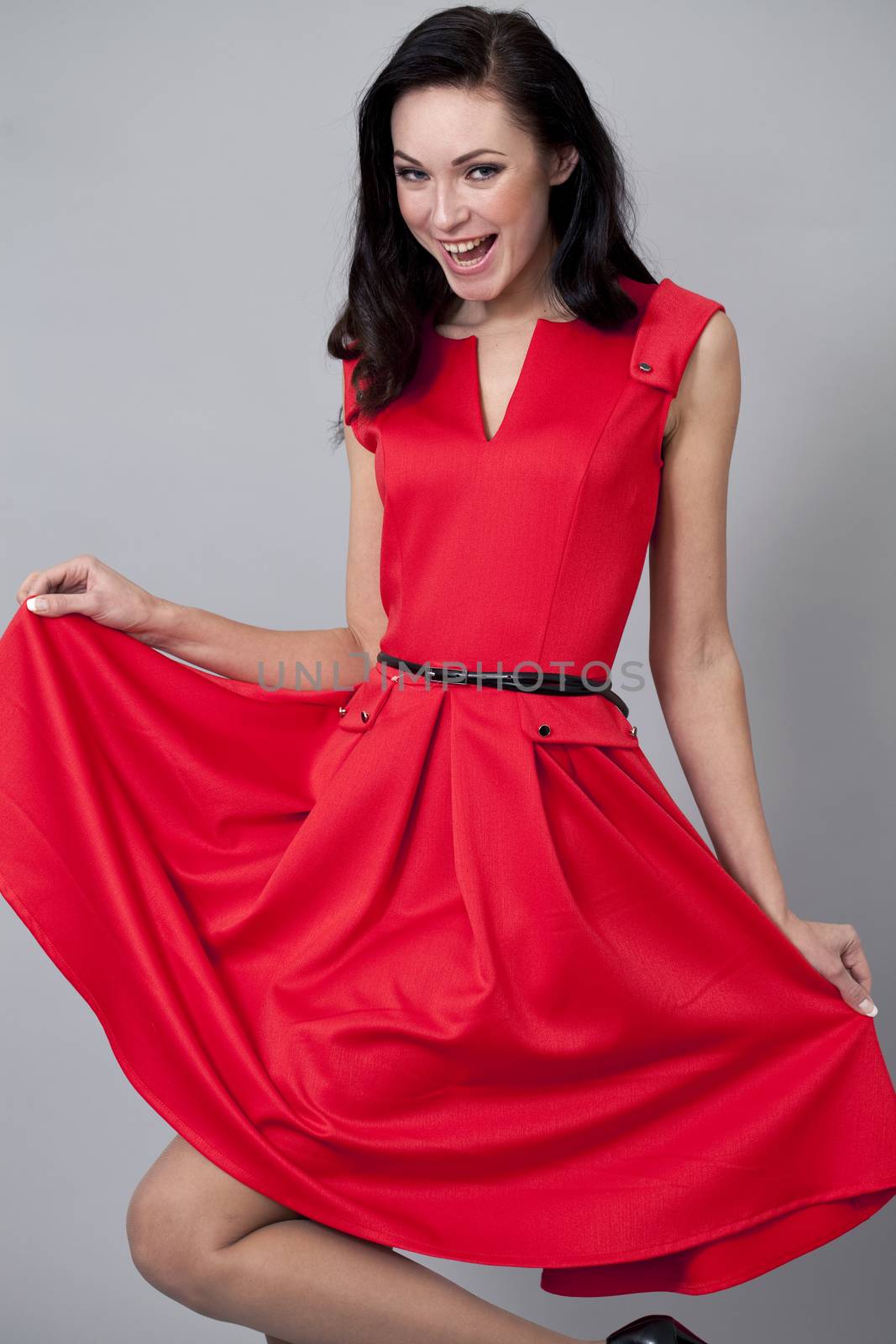 Young beautiful caucasian brunette in red dress posing on grey background