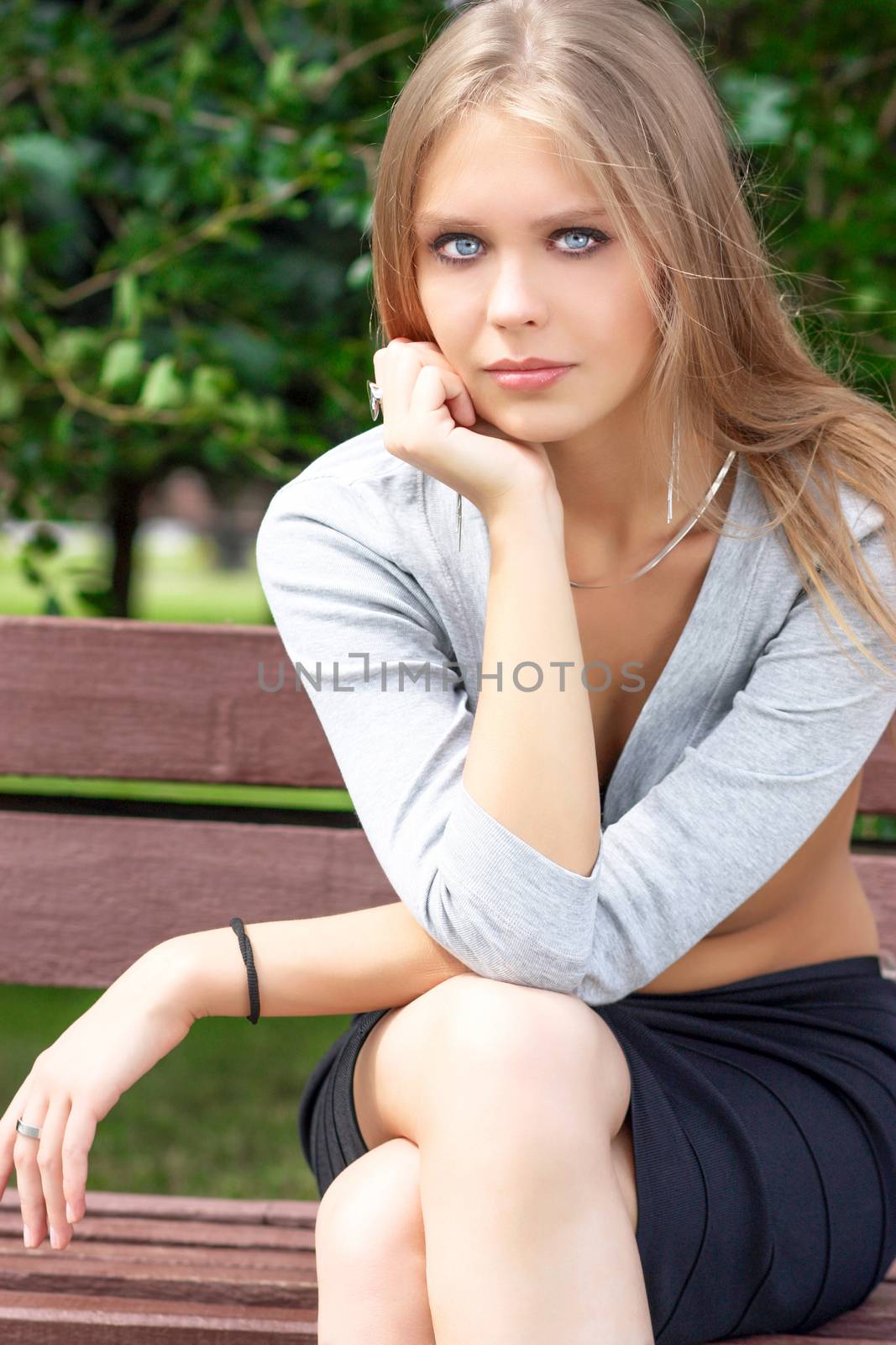 Portrait of blonde young woman sitting on the bench in summer park