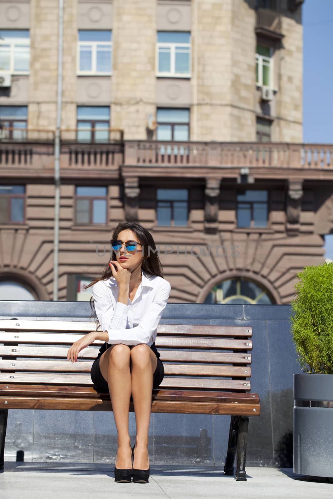 Young beautiful business woman sitting on a bench in the sunny city