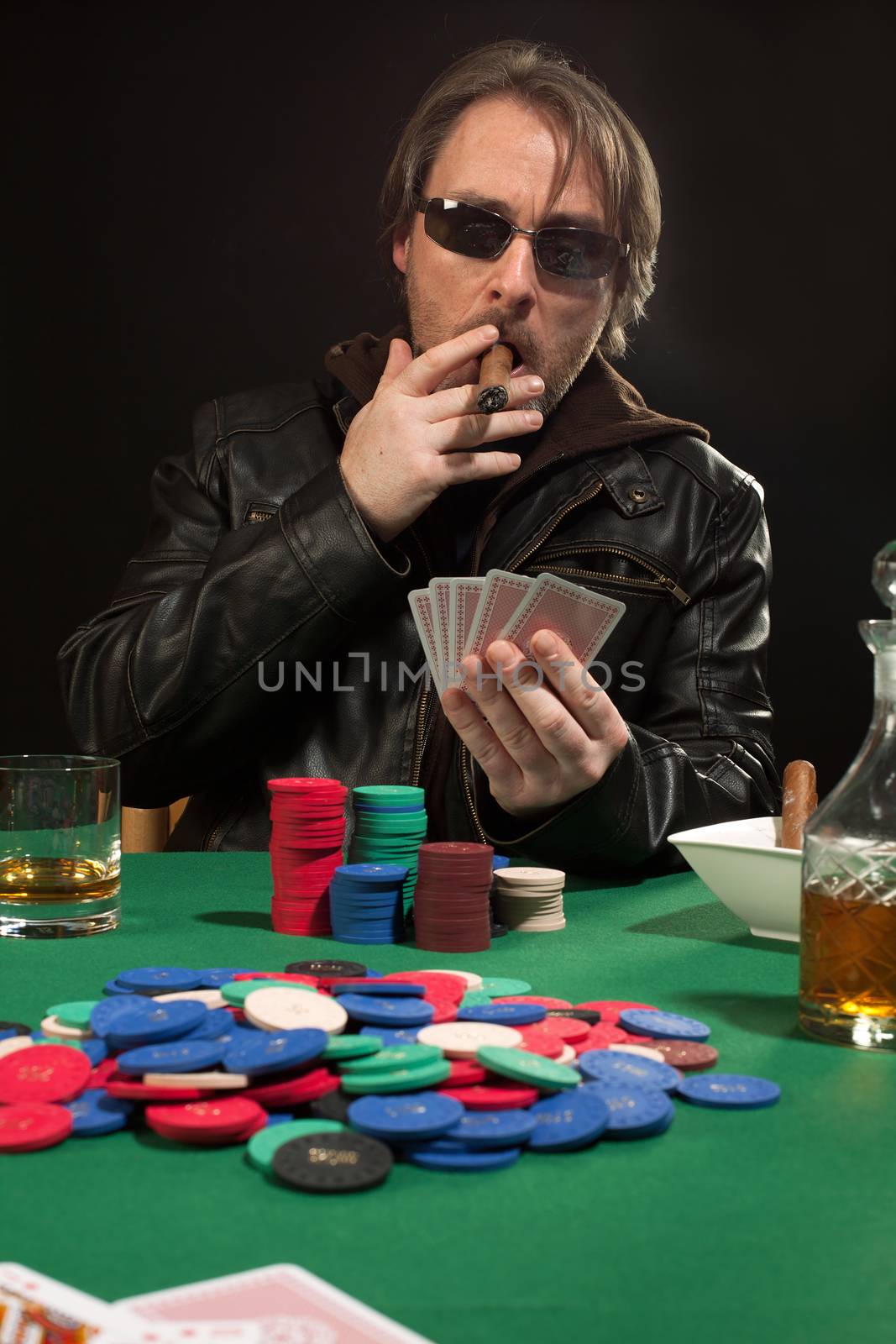 Photo of a man playing poker while wearing sunglasses and smoking a cigar.
