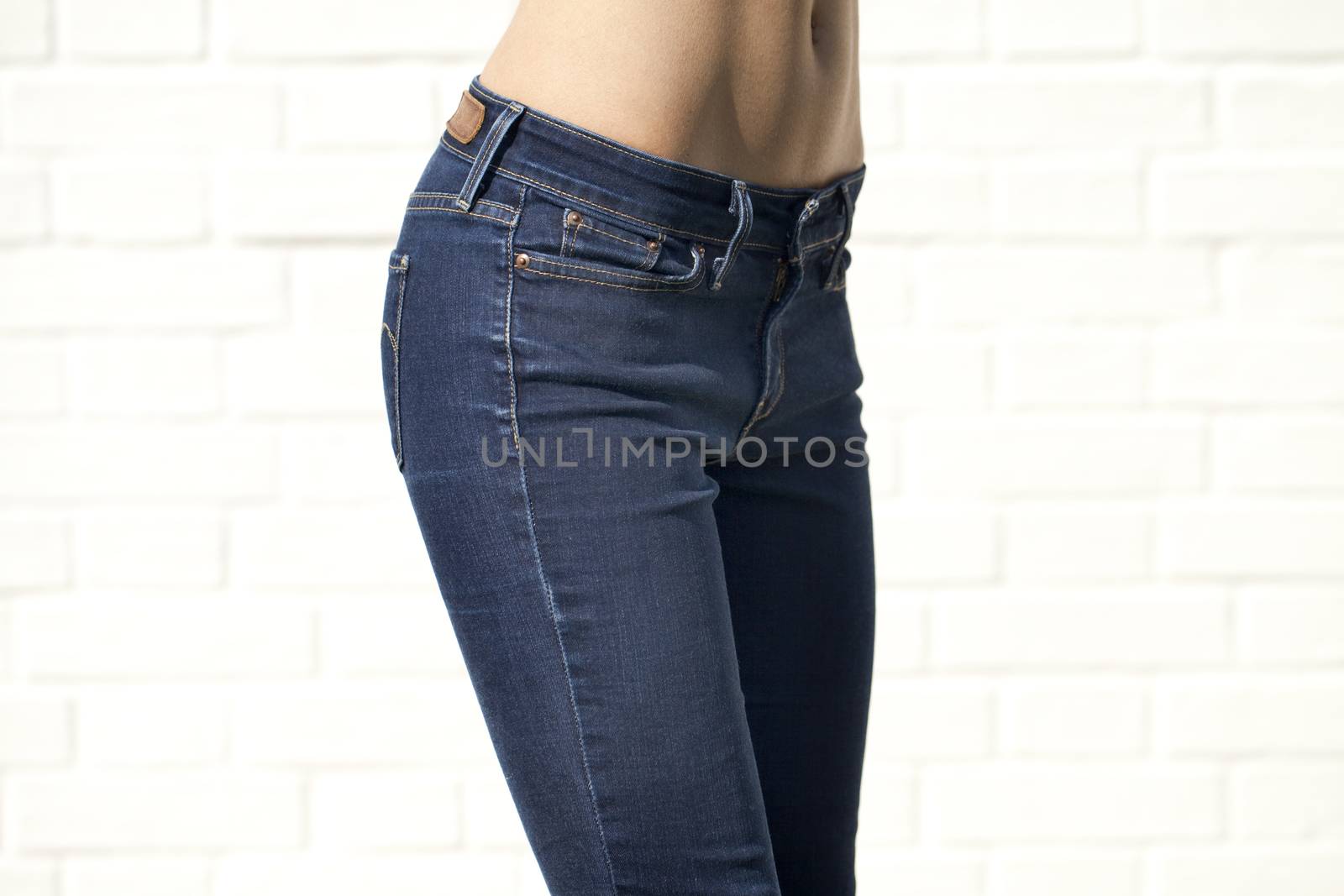 Woman in blue jeans with naked back isolated on white brick wall