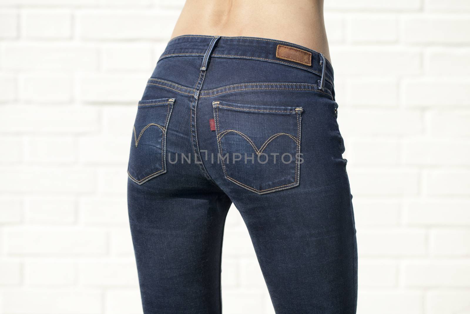 Woman in blue jeans with naked back isolated on white brick wall