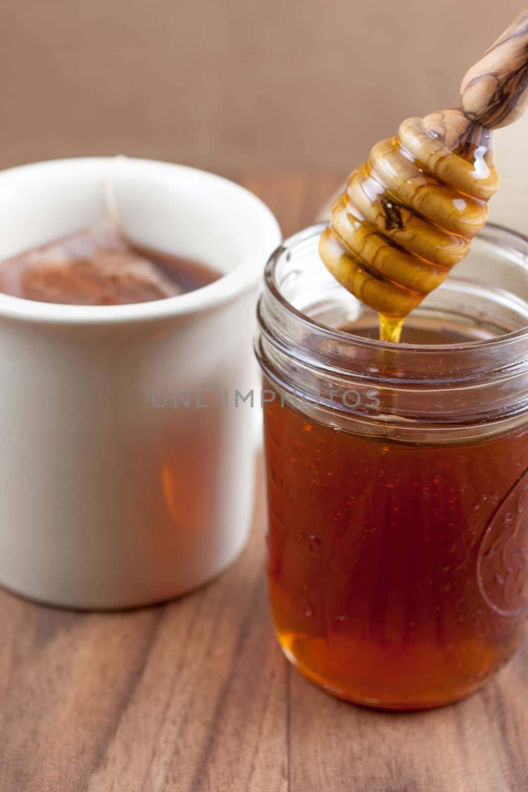 A jar of raw natural honey in a canning jar with a wooden dipper on a wooden table.