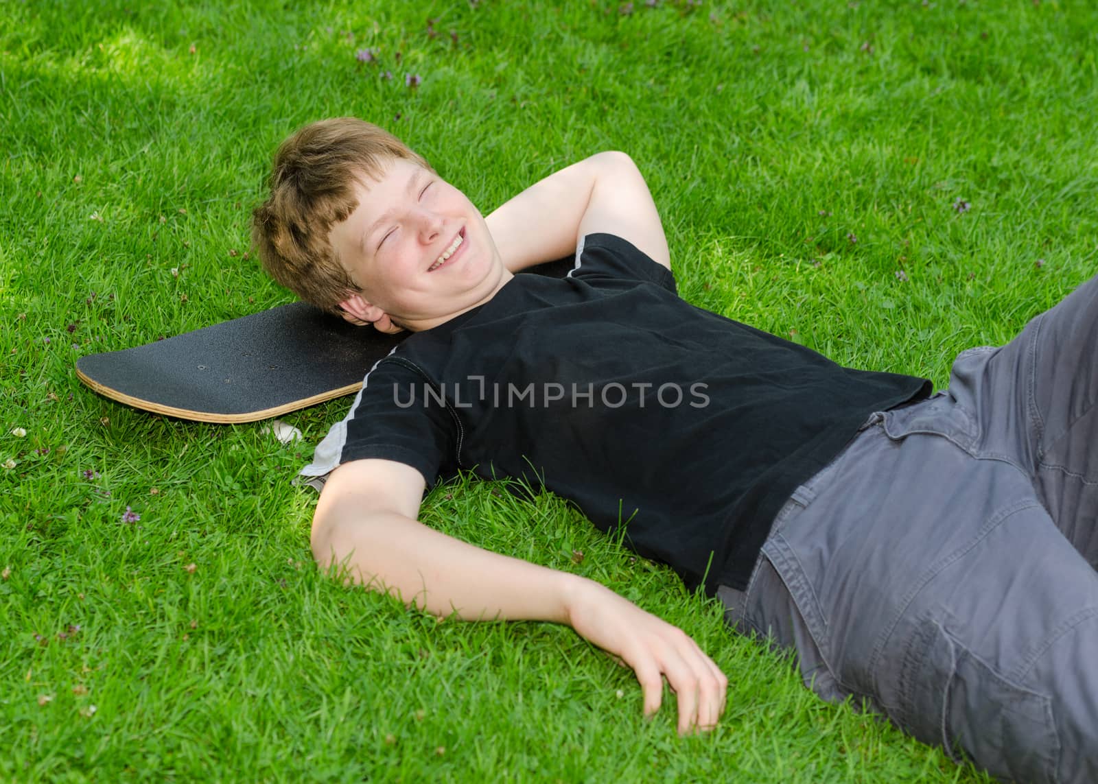Laughing guy relax on skateboard in park grass and rest after an active leisure