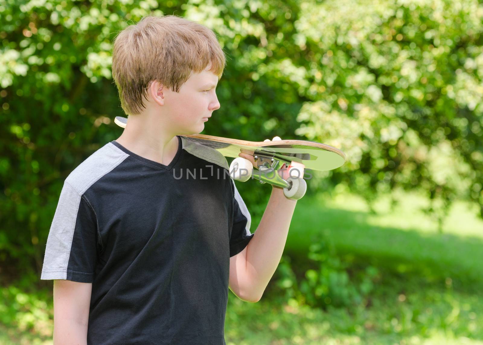 Profile portrait of young skater stand in the park and holding a skateboard on shoulder