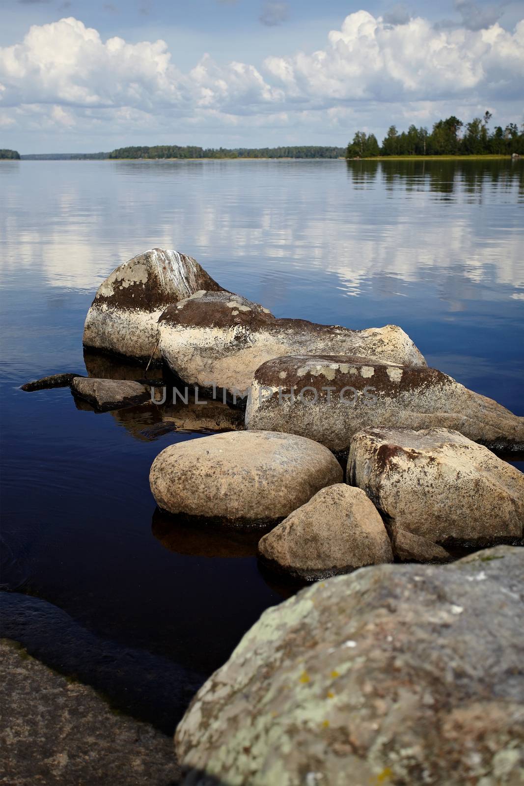 Water landscape with stones. Stones in water. The lake with stones. Beautiful landscape. Water smooth surface and the blue sky with clouds.