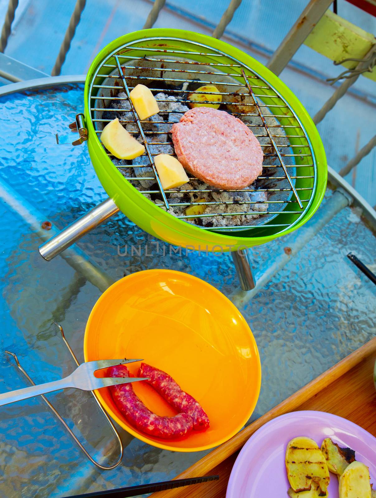 Small BBQ with hamburger and potatoes over table