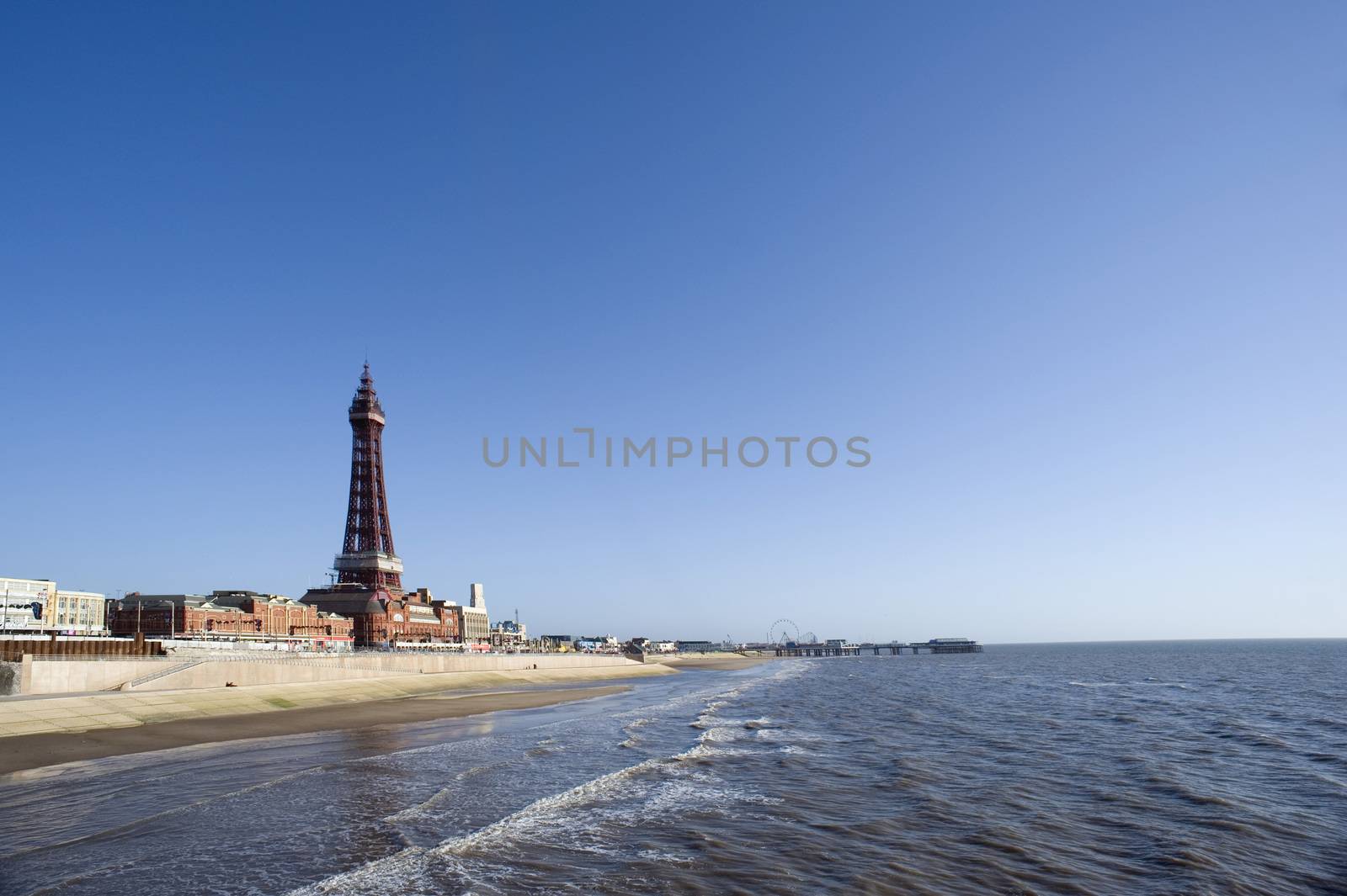 View of Blackpool beachfront with the historic Blackpool Tower, a tourist resort in in Lancashire, England, on a sunny blue sky day