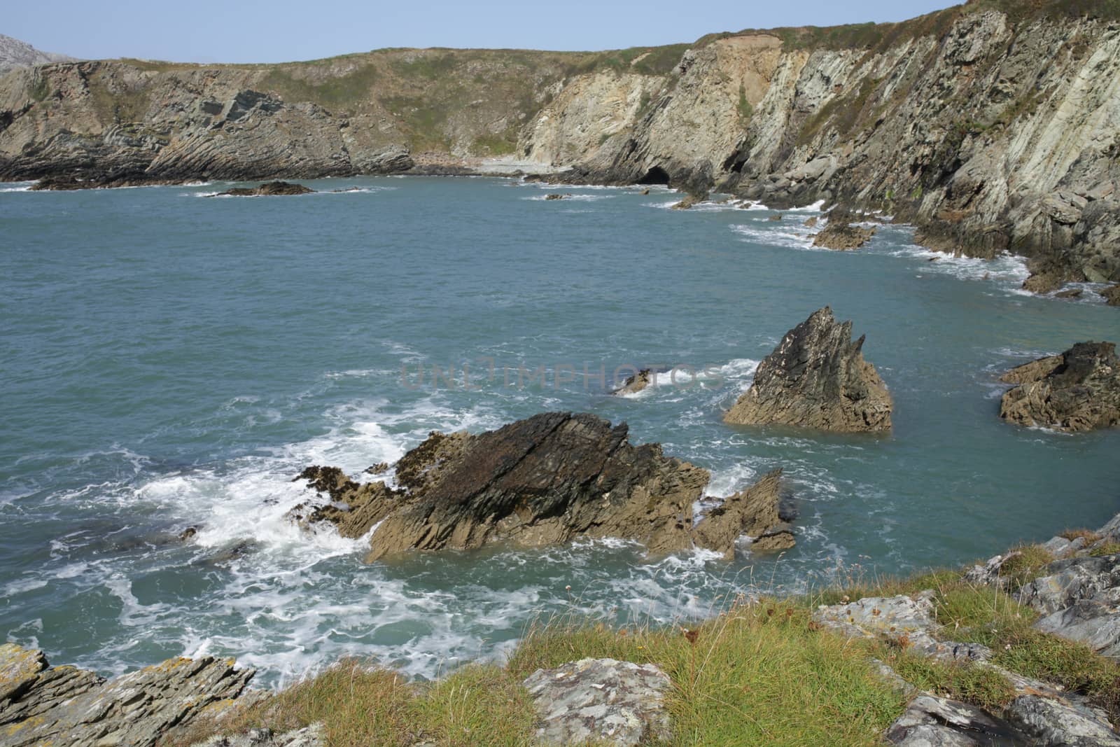 A view from a cliff top across the sea with rocks to cliffs enclosing Abraham's bosom bay, wales coast path, anglesey, Wales, UK.