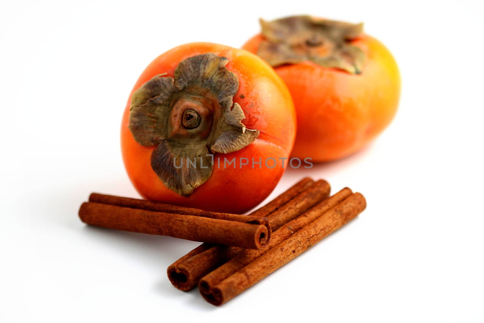 Closeup of persimmons and cinamon on white background.