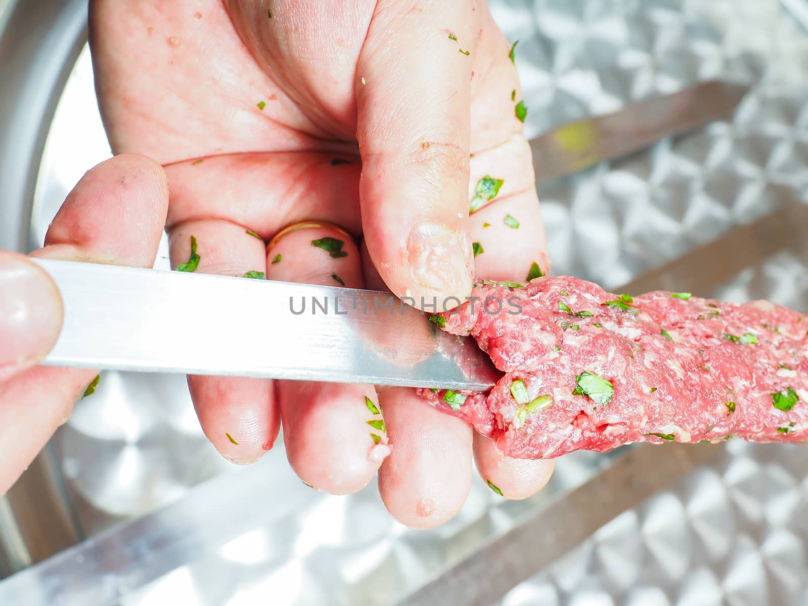 A chef making shish kebab of red meat with parsley over metal plate