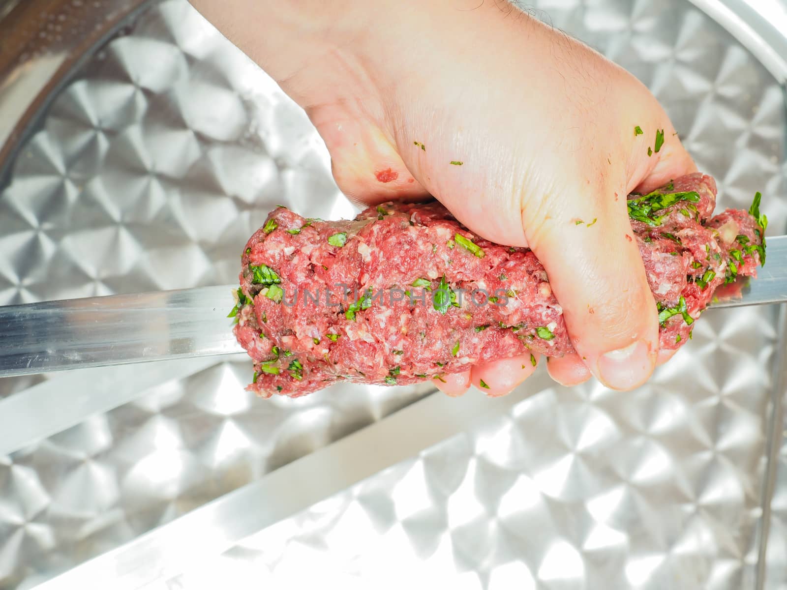 A chef making shish kebab of red meat with parsley over metal plate