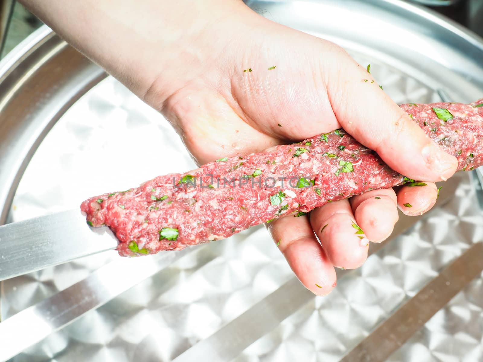 A chef making shish kebab of red meat with parsley over metal plate