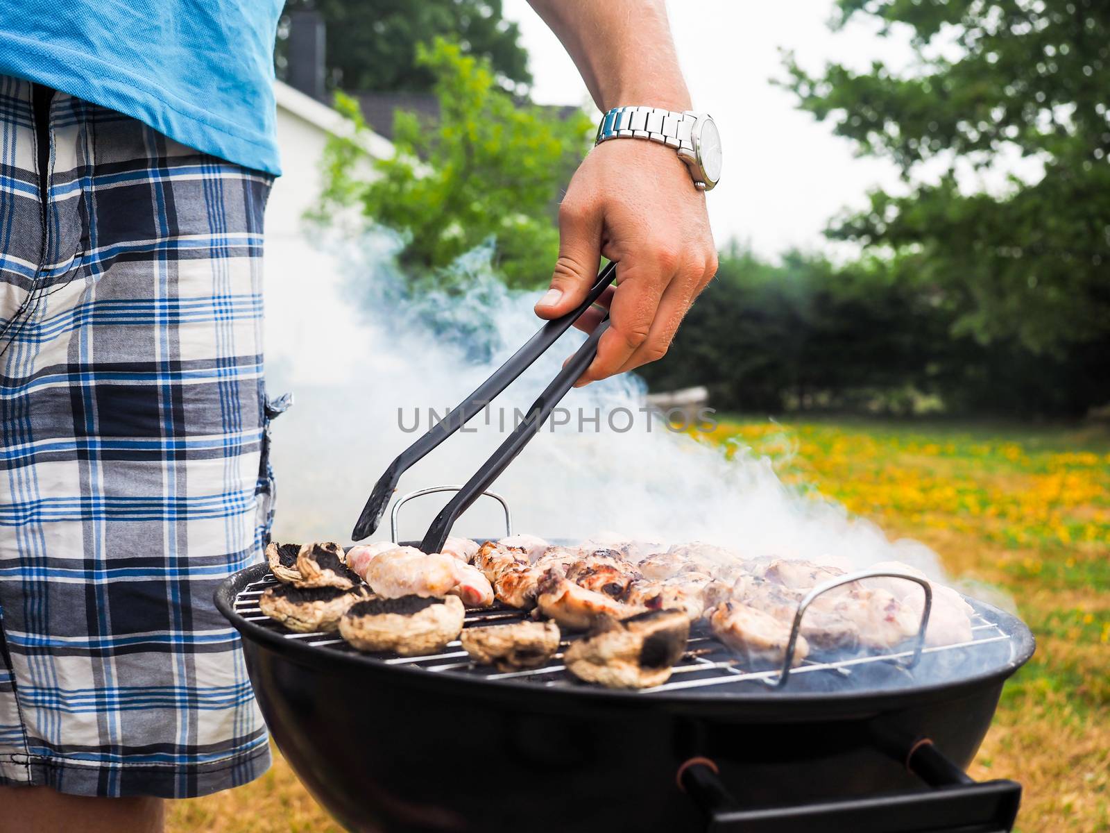 Male person with food tweezers barbequing with lot's of smoke